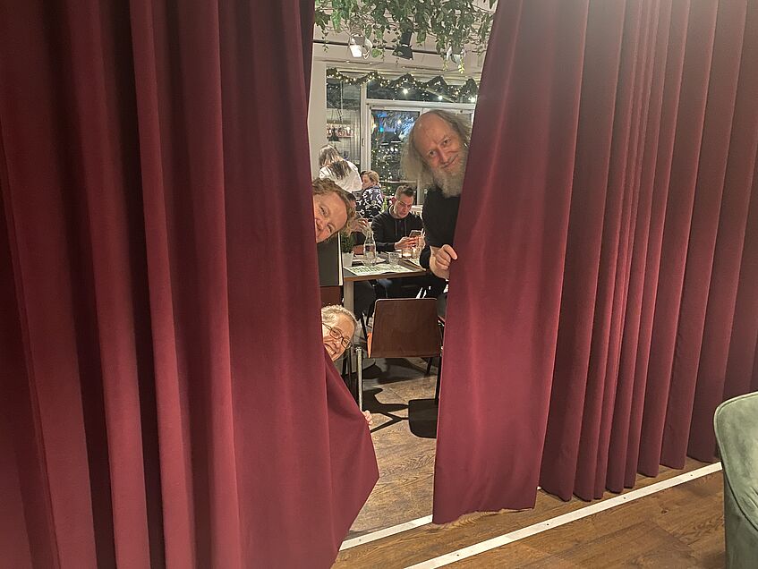 3 people looking out from behind a theater curtain