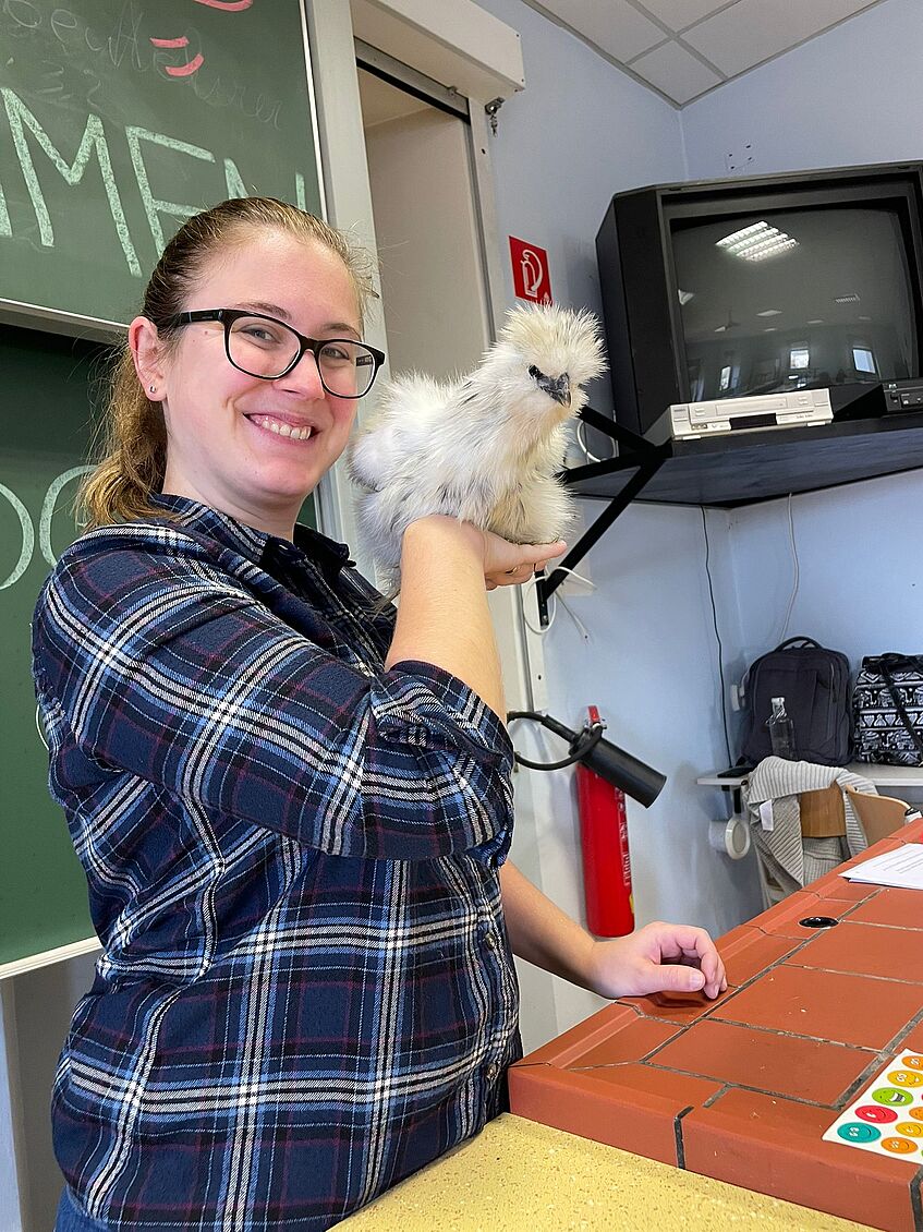 woman in a classroom (teacher), with a chicken in hand