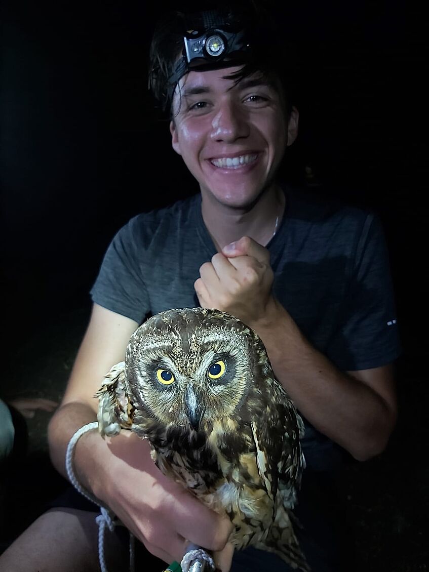 Young male Scientist in the darkness, wearing a headlamp and holding an owl