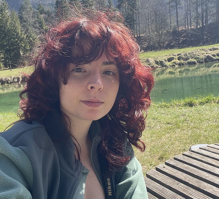 woman with red-brown hair, pond in the background