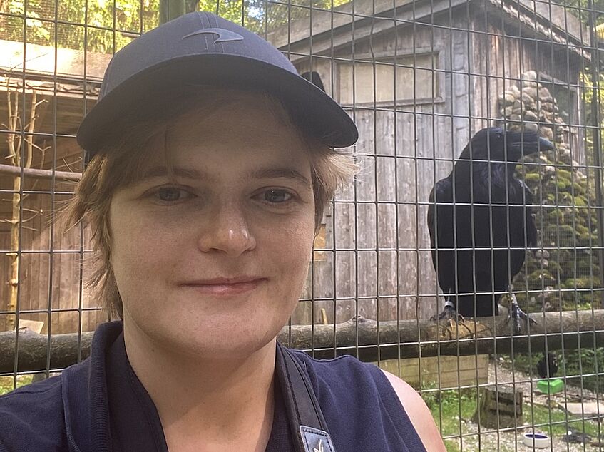 Female scientist with a raven in an enclosure in  the background