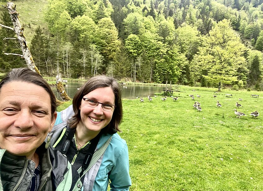 Selfie of two women, a flock of greylag geese in the background